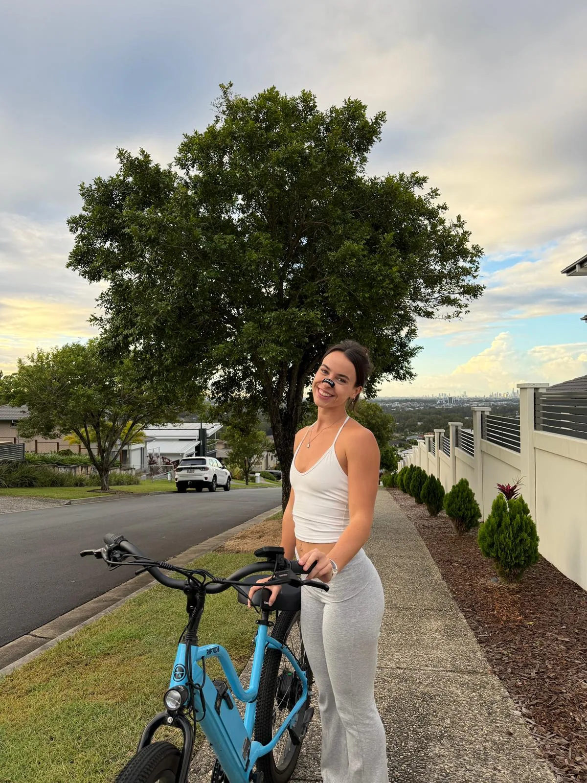 Woman wearing a black RhinoGear nose strip with her e-bike at sunset over Brisbane